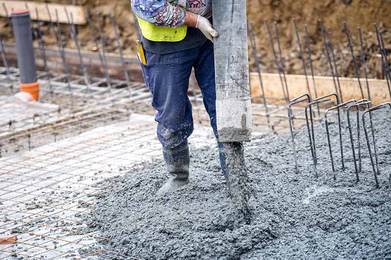 worker in rubber boots pouring concrete from hose